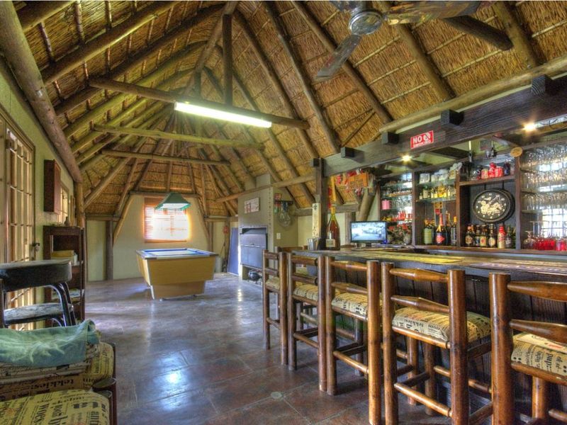 A rustic entertainment bar area featuring a high thatched roof with exposed timber trusses, tiled flooring, and a built-in bar counter.