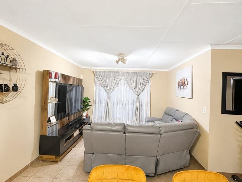 A well-maintained living room featuring neutral wall tones, tiled flooring, and a large sliding glass door providing natural light.