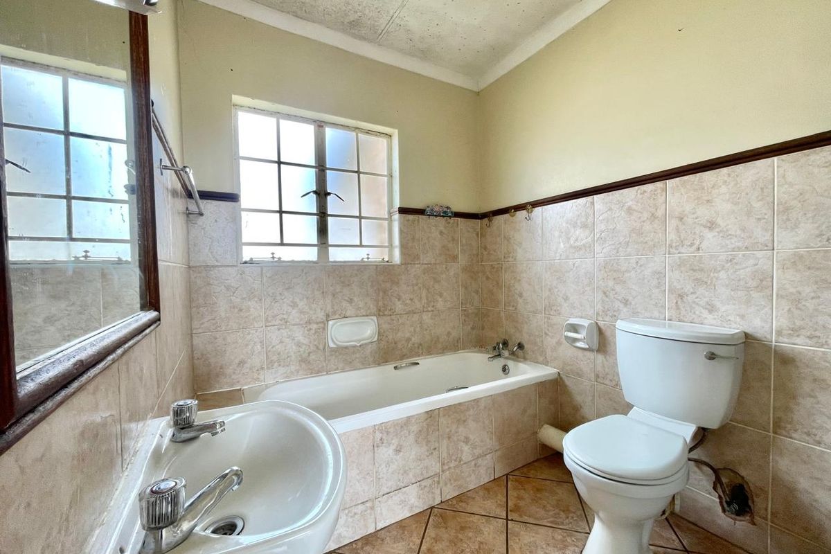 A dated bathroom featuring a built-in bathtub, pedestal basin, and toilet with tiled walls and flooring, requiring cosmetic updates and ceiling repairs.