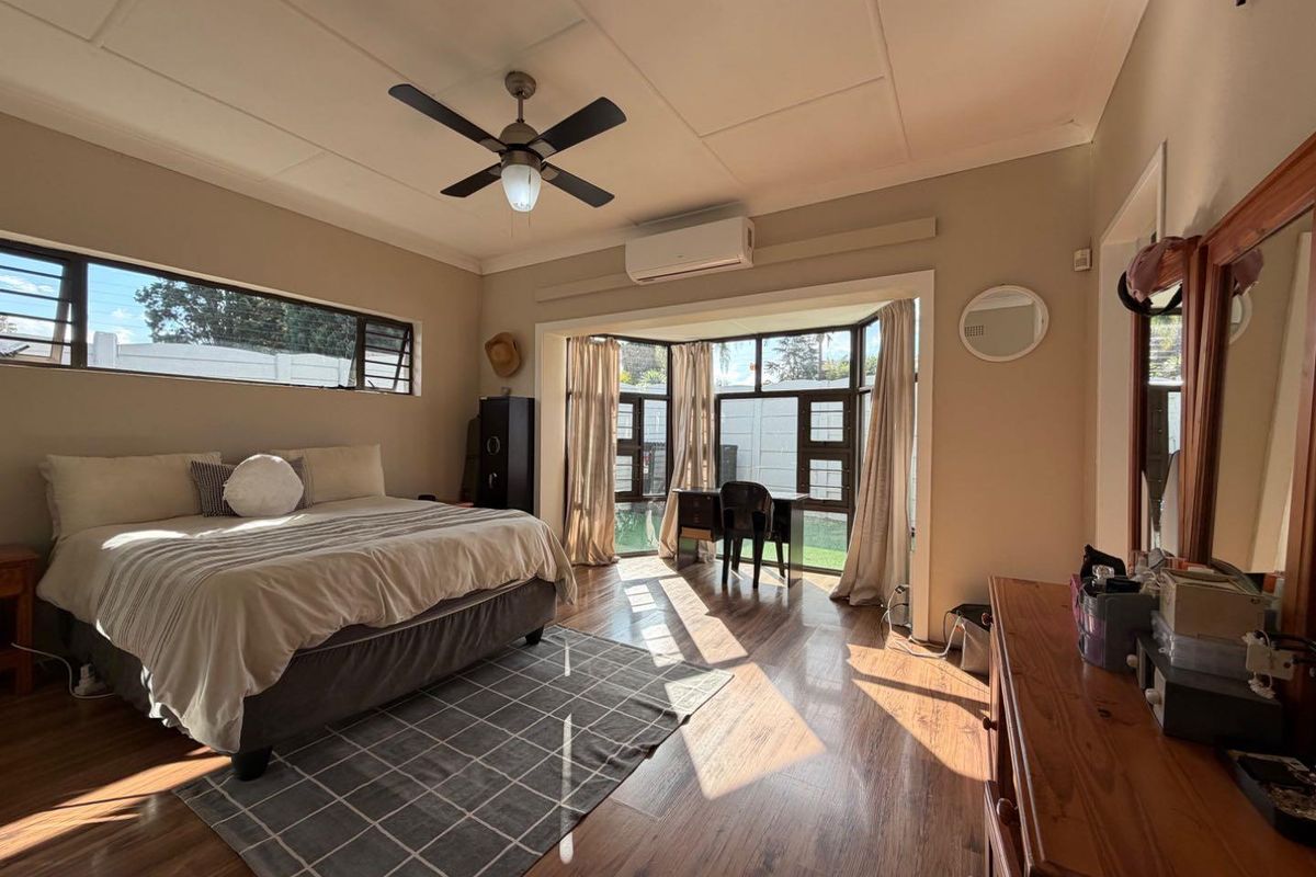 Spacious bedroom featuring wood-look flooring, a ceiling fan, split-system air conditioning, and large windows providing ample natural light.