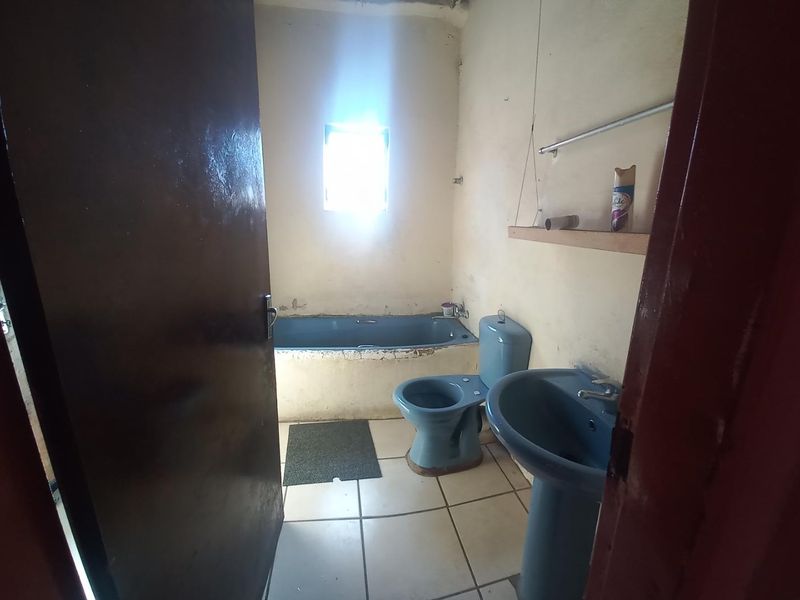 A dated bathroom featuring a blue bathtub, toilet, and pedestal basin with tiled flooring, requiring cosmetic updates and renovation.