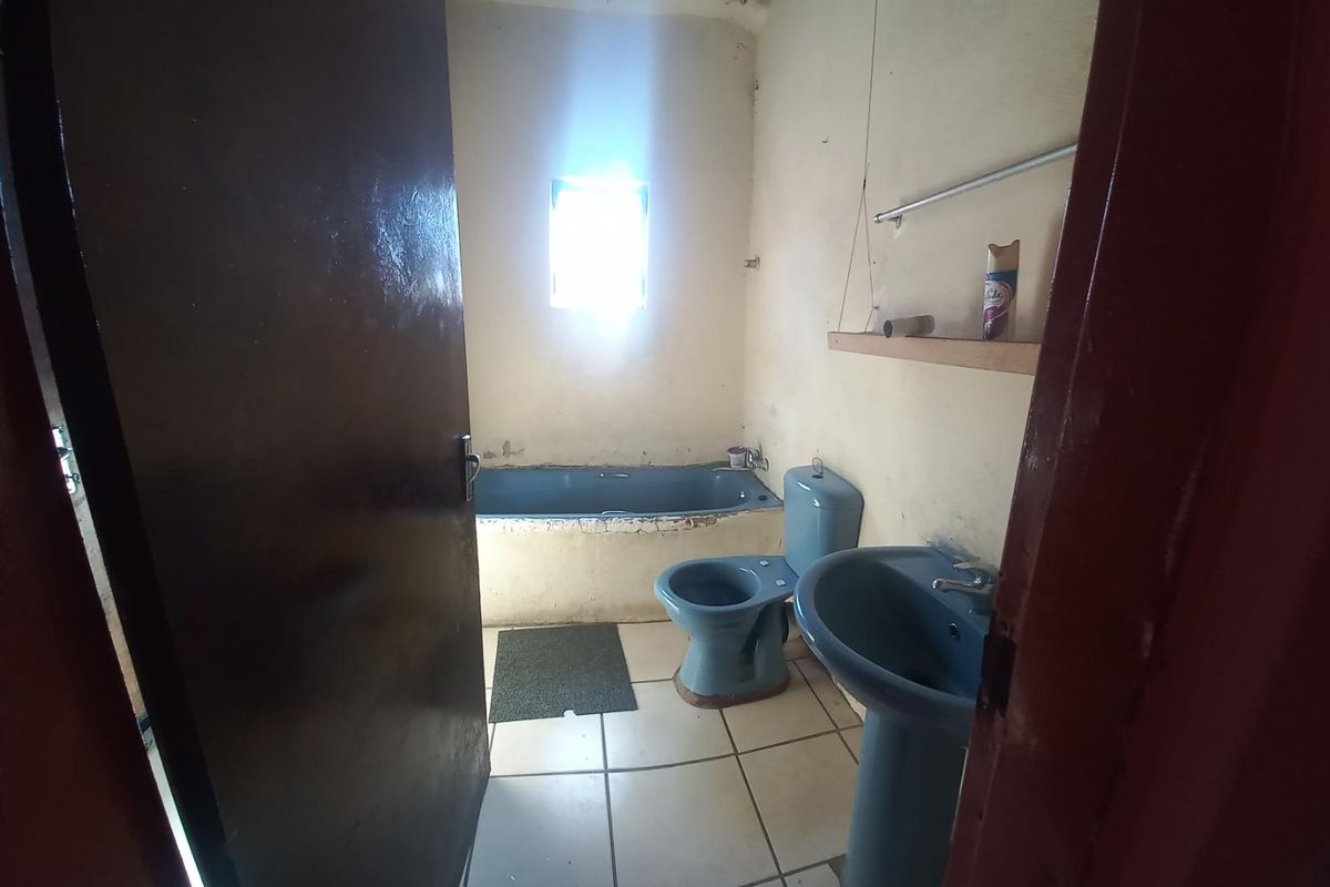 A dated bathroom featuring a blue bathtub, toilet, and pedestal basin with tiled flooring, requiring cosmetic updates and renovation.