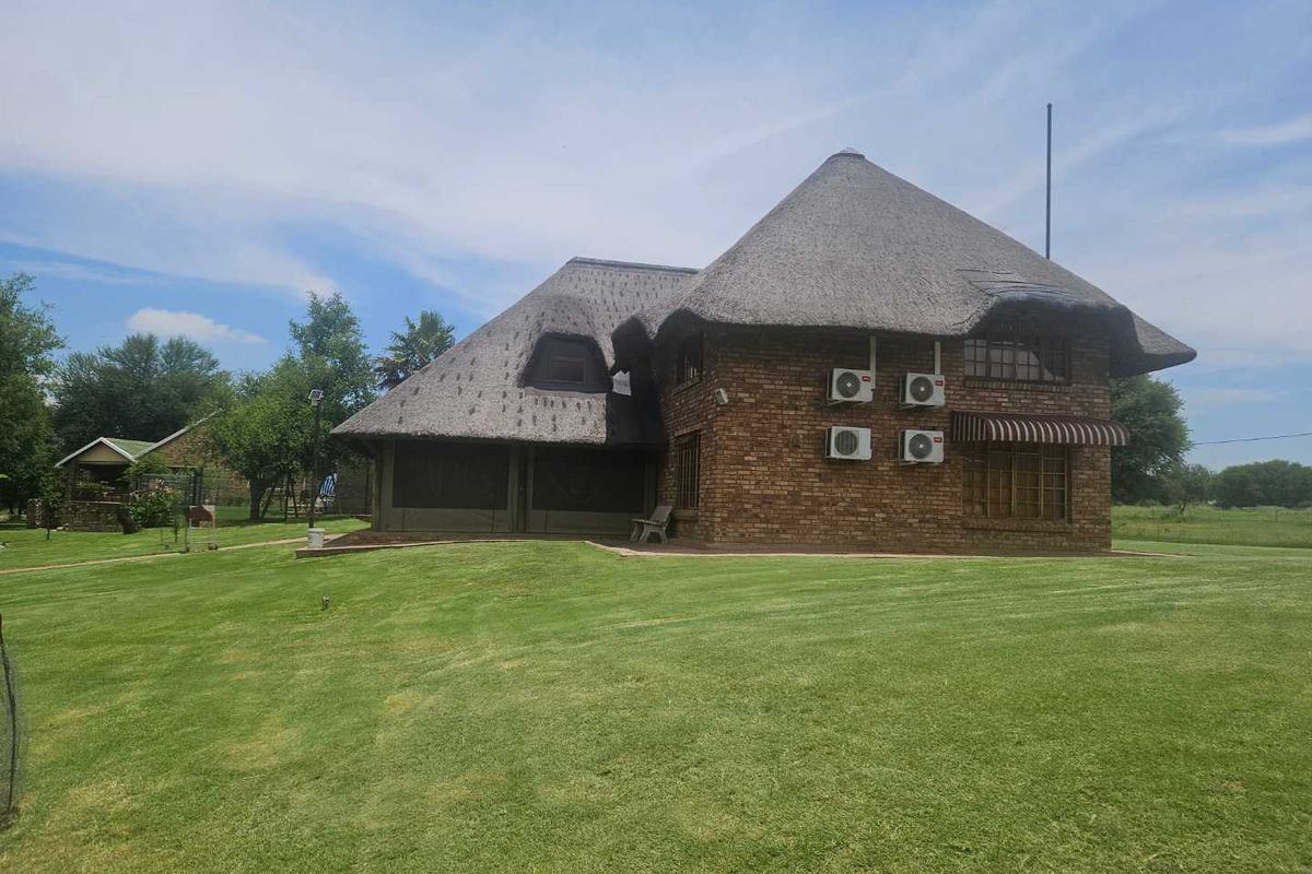A traditional thatched-roof house featuring brick exterior walls, set within a spacious, well-maintained green lawn area.