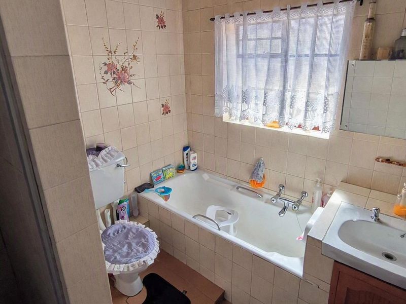 A functional bathroom featuring a bathtub, toilet, and vanity basin with neutral wall tiling and a window for natural light.