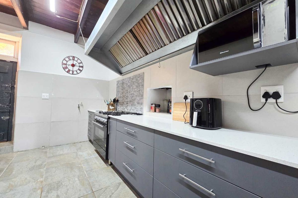 Modern kitchen featuring grey cabinetry, stone countertops, a gas stove with a large extractor hood, and tiled flooring under a vaulted timber ceiling.