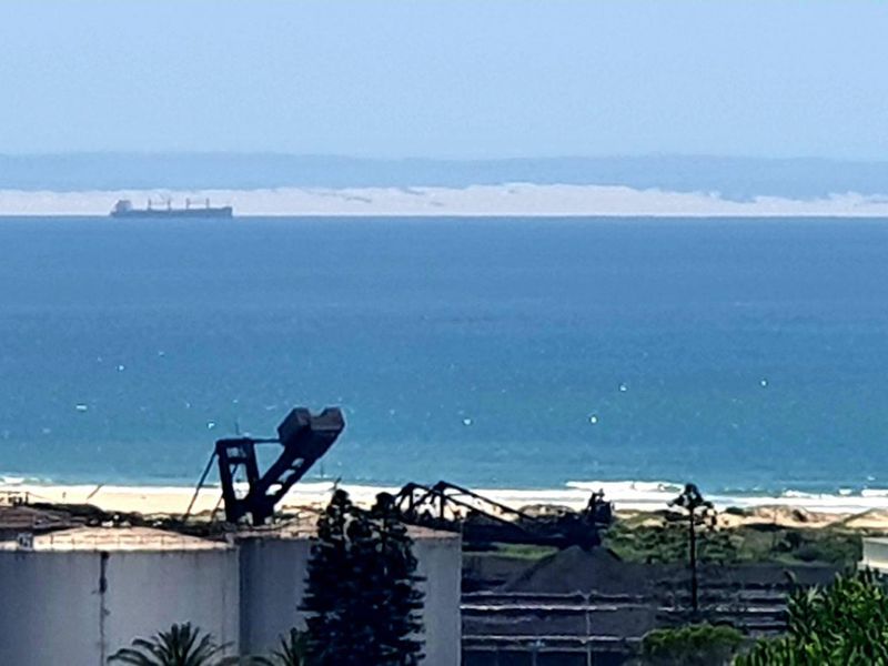 A distant coastal view overlooking industrial infrastructure, storage tanks, and the ocean horizon.
