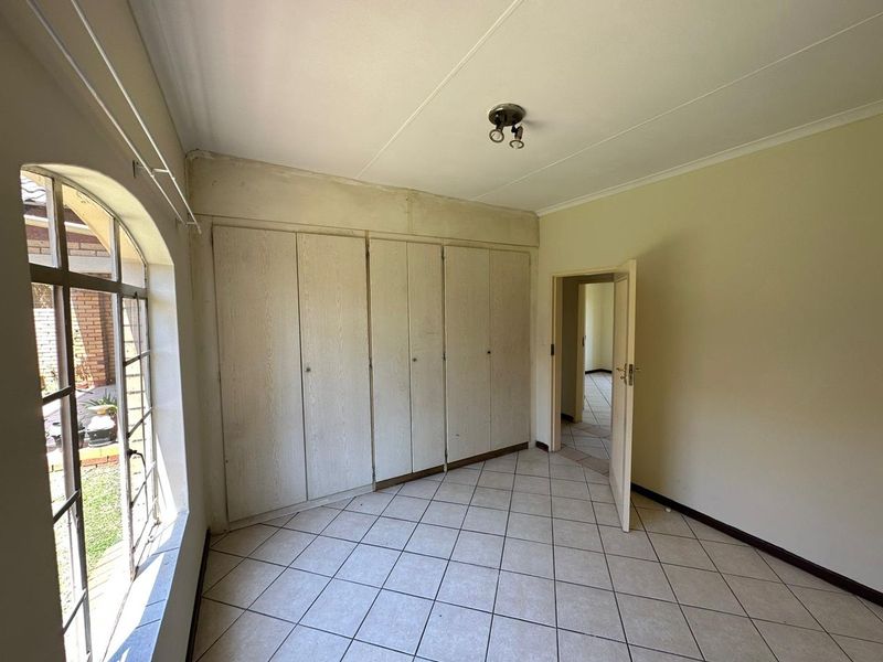 An empty bedroom featuring tiled flooring, built-in cupboards, and an arched window, requiring cosmetic updates to the walls and finishes.