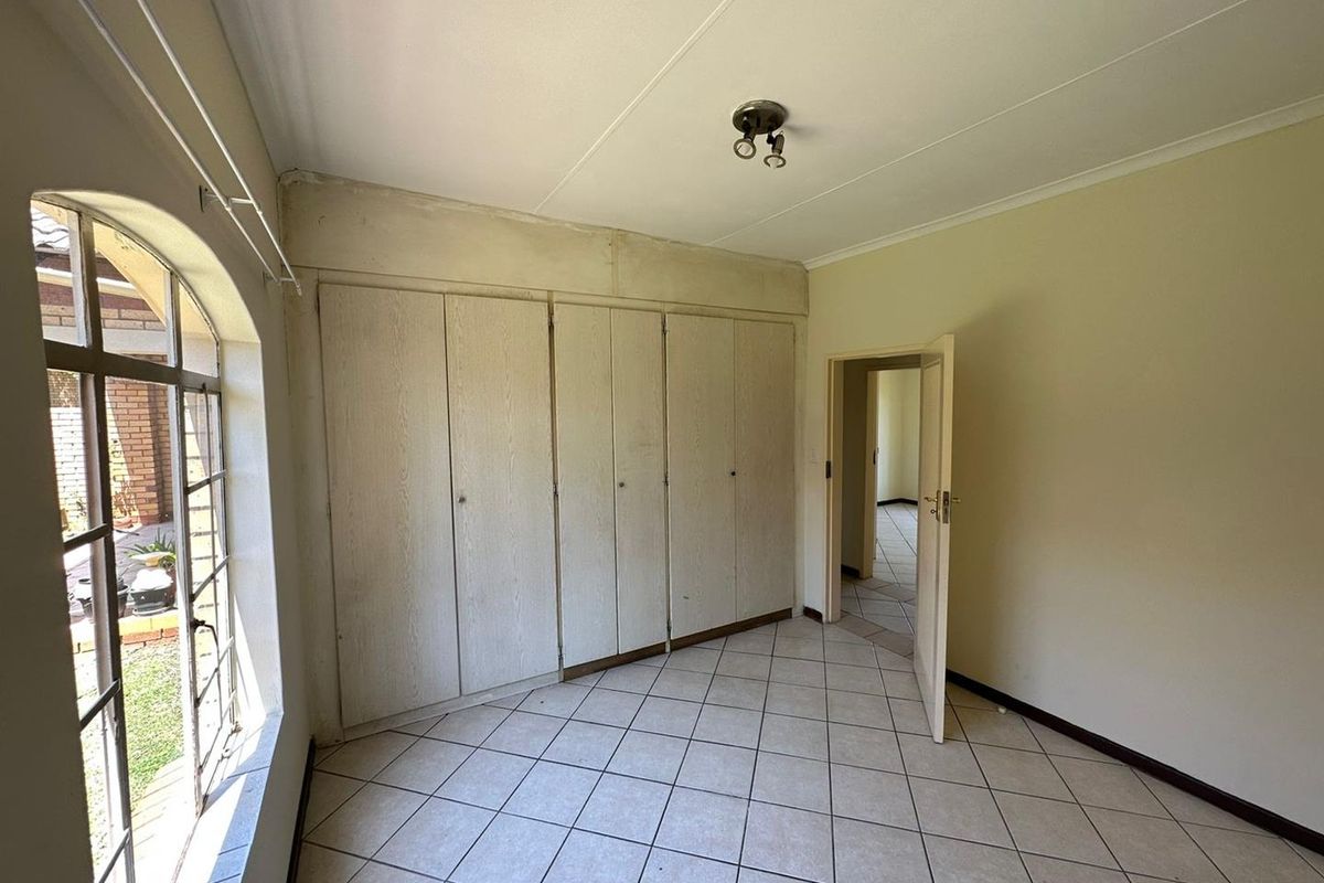 An empty bedroom featuring tiled flooring, built-in cupboards, and an arched window, requiring cosmetic updates to the walls and finishes.