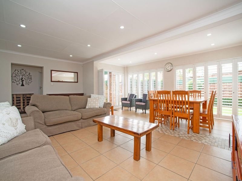 Spacious open-plan living and dining area featuring neutral tiled flooring, recessed lighting, and large folding glass doors with white plantation shutters.