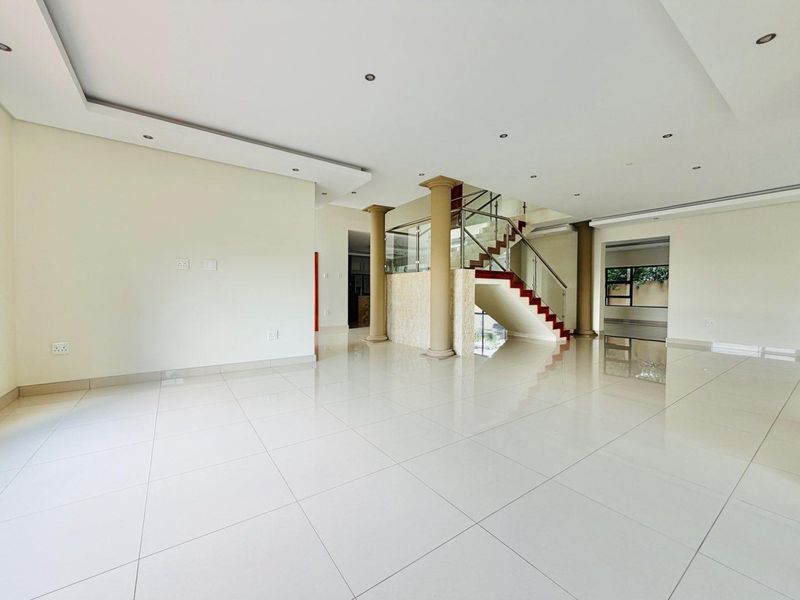 Spacious open-plan living area featuring polished porcelain tiles, a modern staircase with glass balustrades, decorative columns, and a contemporary dropped ceiling design.