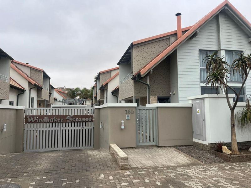 Front view of a townhouse complex entrance featuring a secure gated access, paved driveway, and modern architectural facade with tiled roofing.