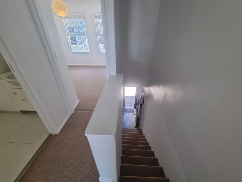 A view from the upper landing looking down the staircase towards the entrance, with adjacent carpeted bedroom area and tiled bathroom access.
