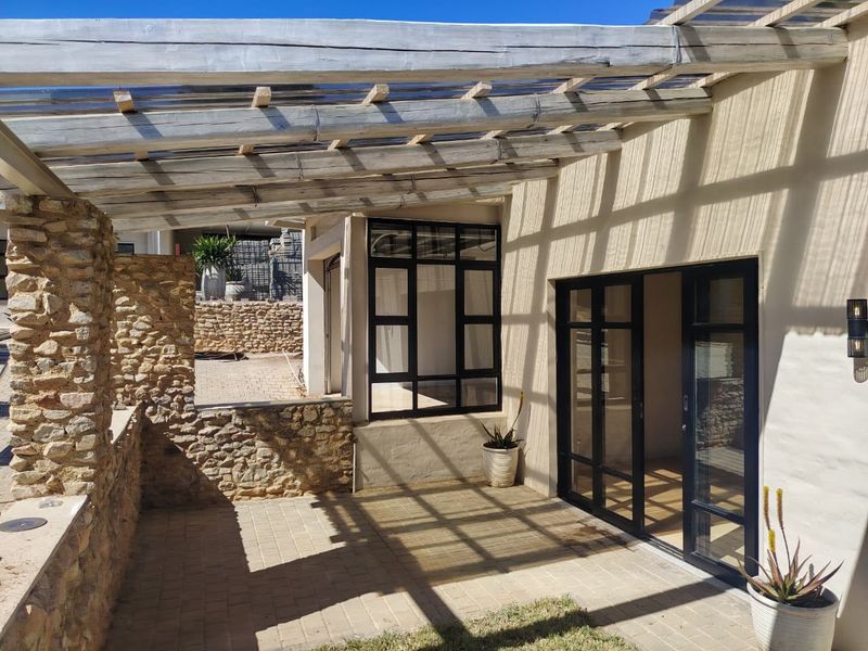 A covered outdoor patio featuring a timber pergola, stone-clad walls, and black aluminium framed glass doors leading into the interior.