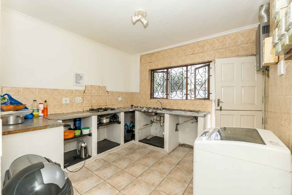 A functional kitchen area featuring tiled walls, built-in concrete counters, a gas hob, and a dedicated space for laundry appliances.