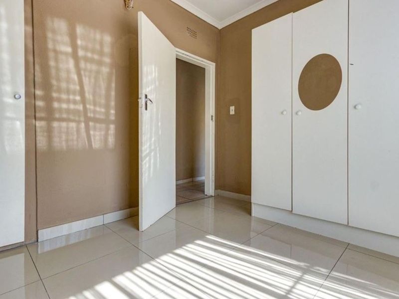 An empty bedroom featuring neutral wall tones, tiled flooring, and built-in cupboards, offering a clean and versatile space ready for personalization.
