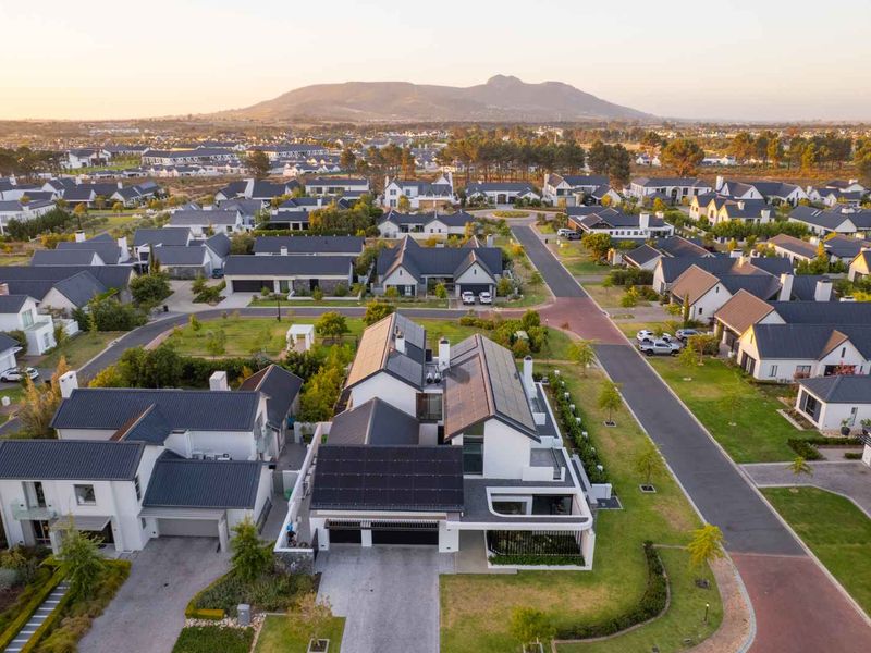 Aerial view of a modern residential property featuring solar panels, a tiled roof, and a landscaped garden within a well-maintained estate.