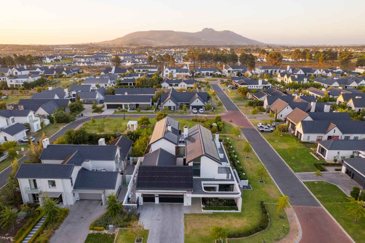 Aerial view of a modern residential property featuring solar panels, a tiled roof, and a landscaped garden within a well-maintained estate.
