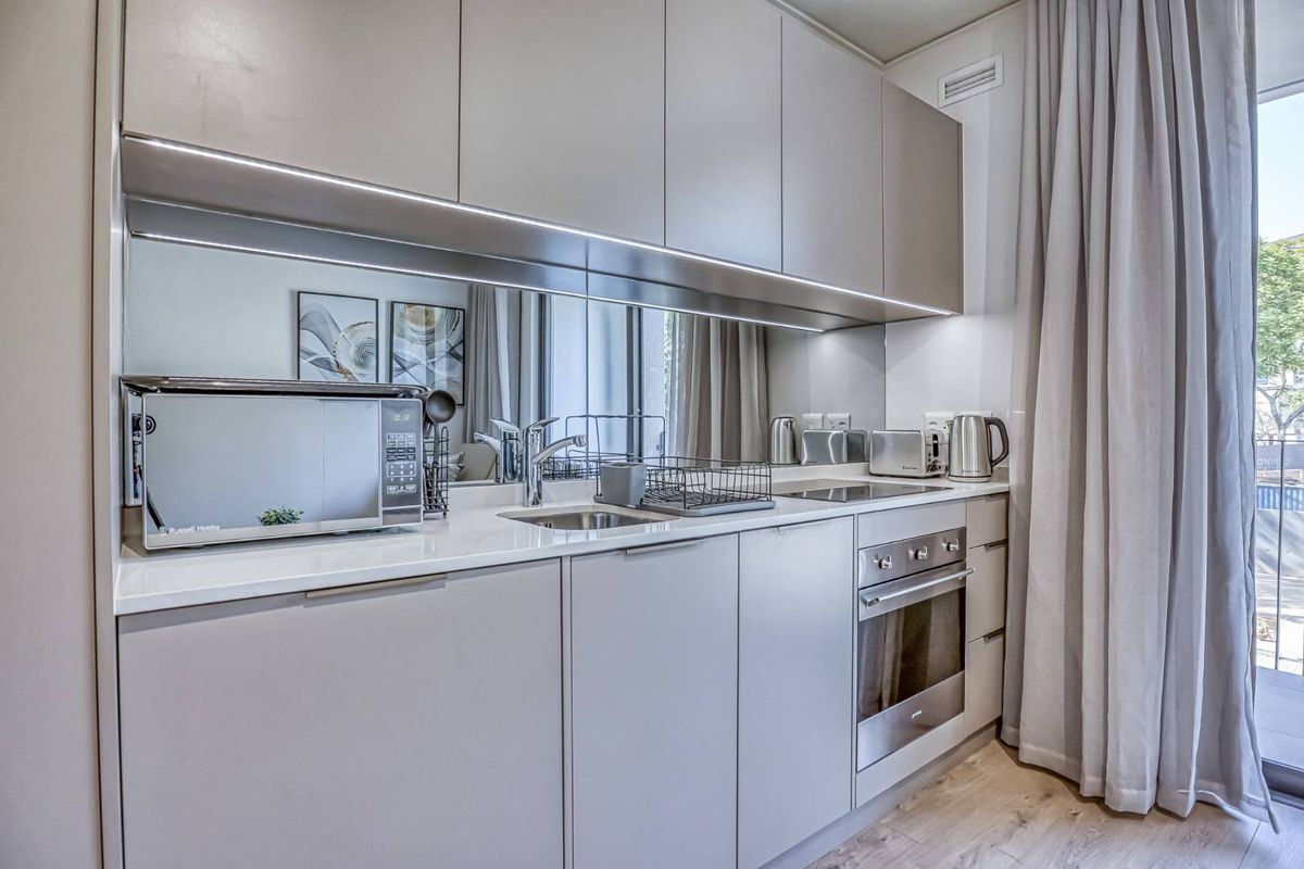 Modern compact kitchen featuring sleek handleless cabinetry, integrated oven, cooktop, and a mirrored backsplash, providing a clean and contemporary aesthetic.