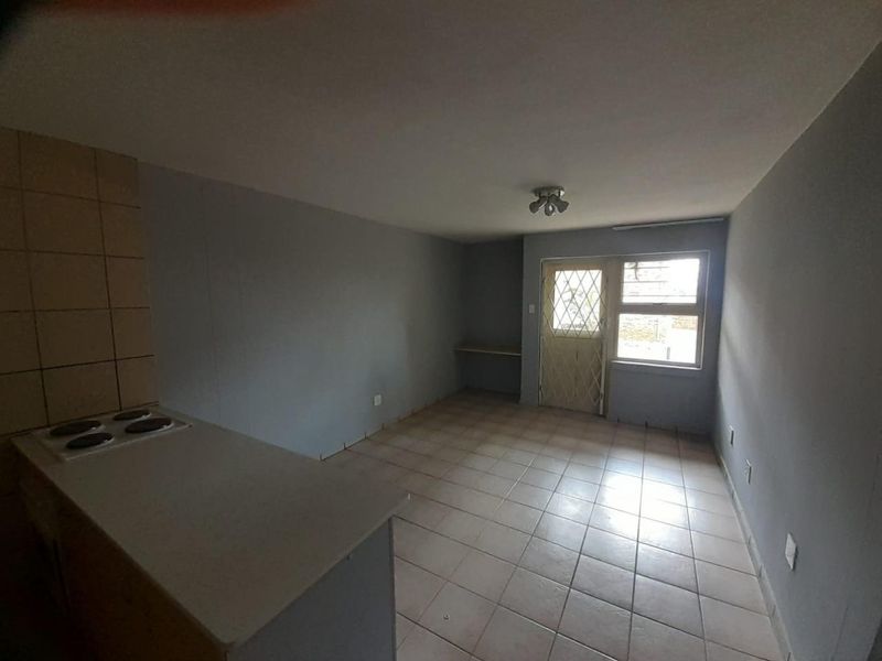 An empty open-plan living and kitchen area featuring tiled flooring, a built-in electric hob, and a security gate leading to the exterior.