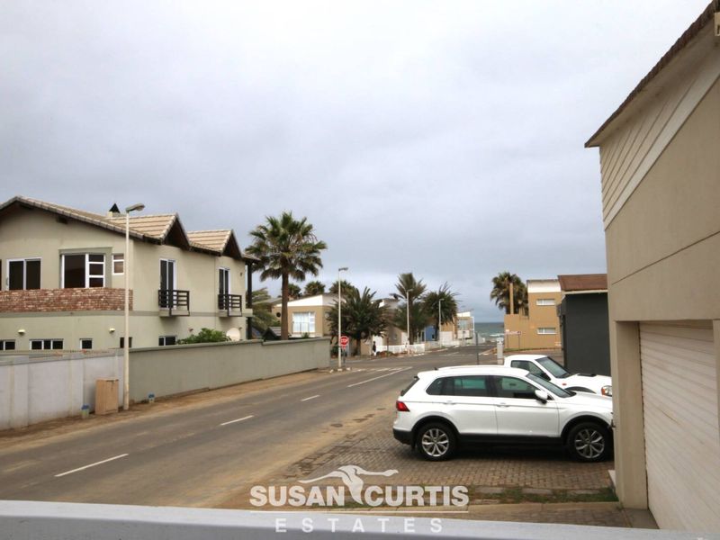 A street view showing the neighbourhood approach and surrounding residential properties with a glimpse of the ocean in the distance.