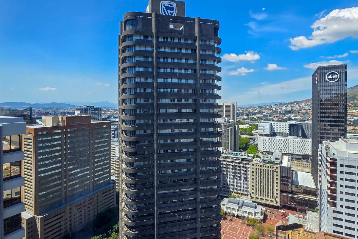 An elevated aerial view of a prominent high-rise apartment building featuring wrap-around balconies within a dense urban city center.