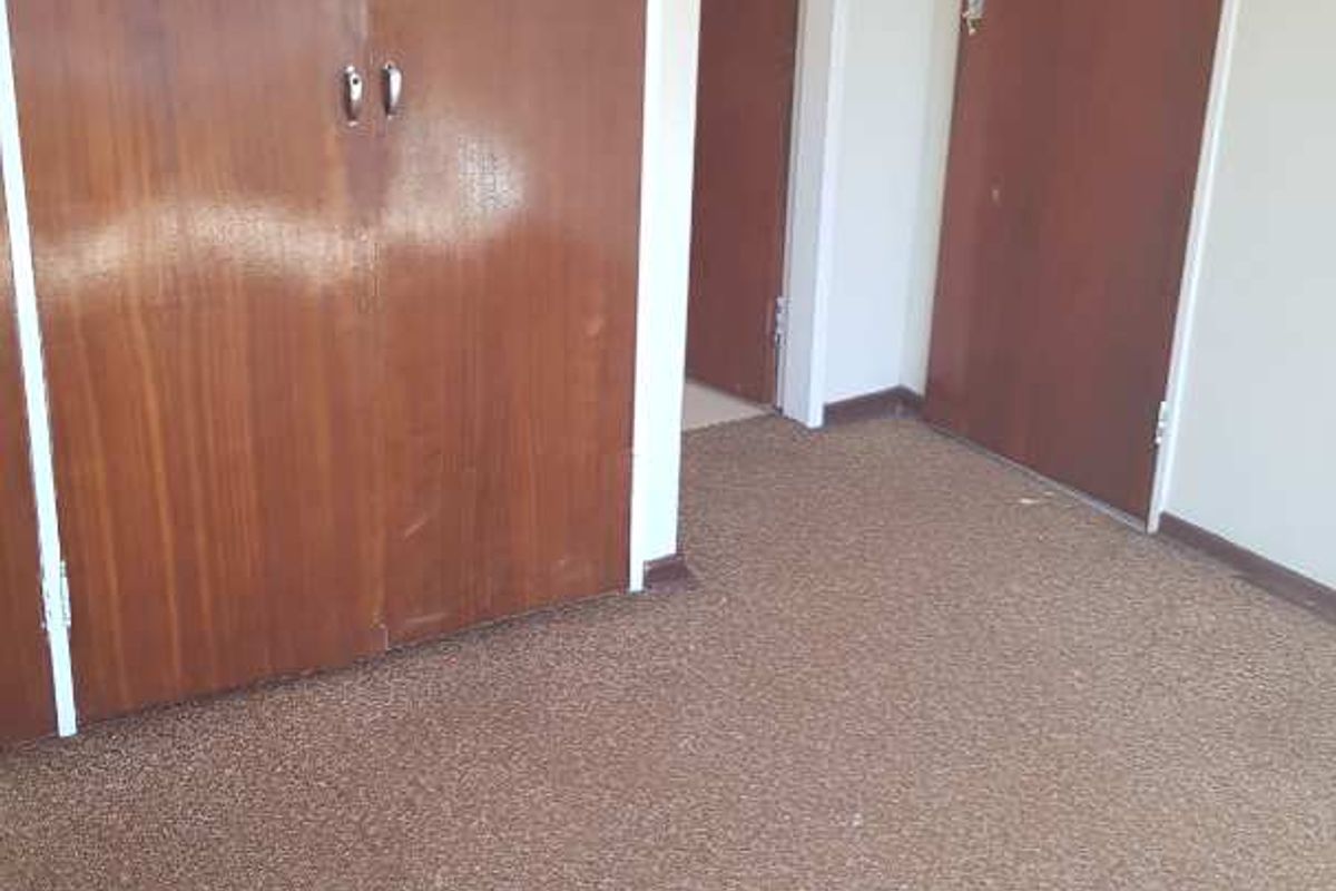 An empty bedroom featuring built-in wooden cupboards, carpeted flooring, and standard internal doors.