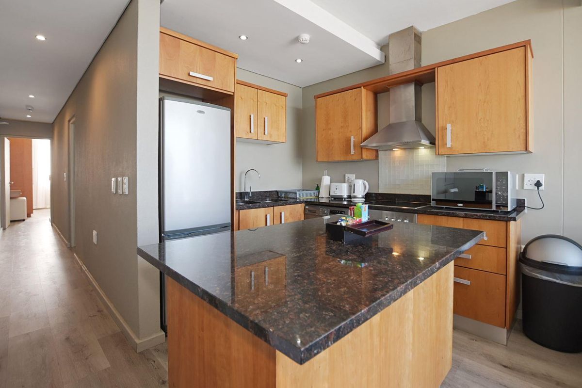 A functional kitchen featuring wooden cabinetry, dark granite countertops, a central island, and stainless steel extractor fan.