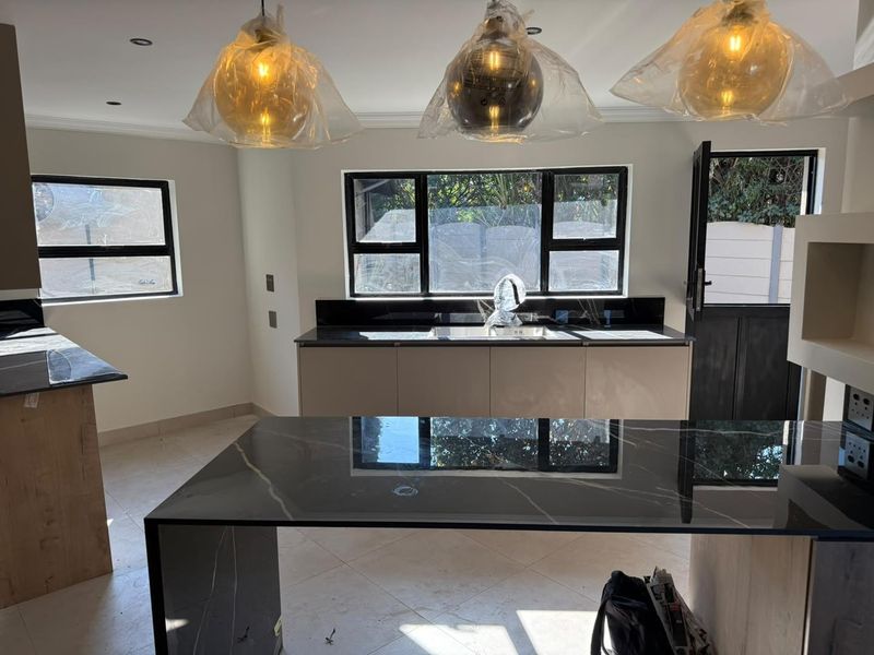 Modern kitchen featuring a large stone-topped island, sleek cabinetry, and black-framed windows, offering a clean and contemporary aesthetic.