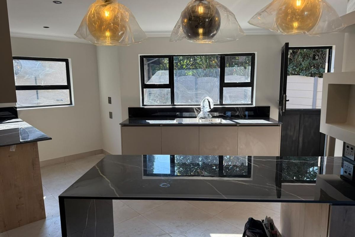 Modern kitchen featuring a large stone-topped island, sleek cabinetry, and black-framed windows, offering a clean and contemporary aesthetic.