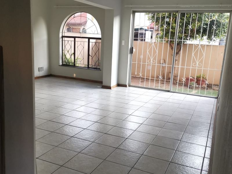 Spacious, empty living area featuring neutral tiled flooring, an arched window, and sliding glass doors leading to the rear garden.
