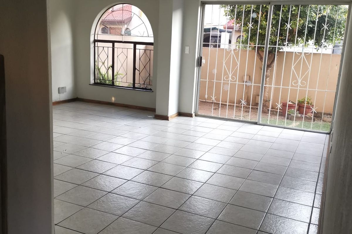Spacious, empty living area featuring neutral tiled flooring, an arched window, and sliding glass doors leading to the rear garden.