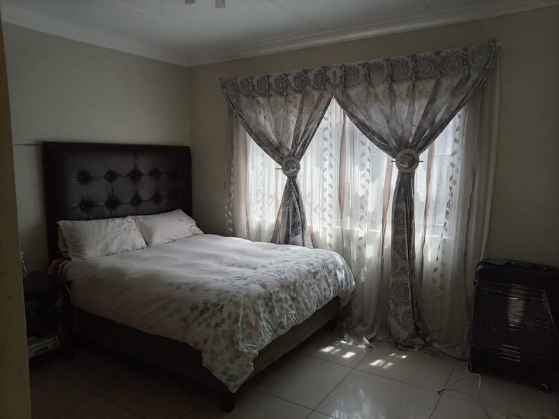 A bedroom featuring tiled flooring and decorative cornicing, illuminated by natural light through a window with curtains.