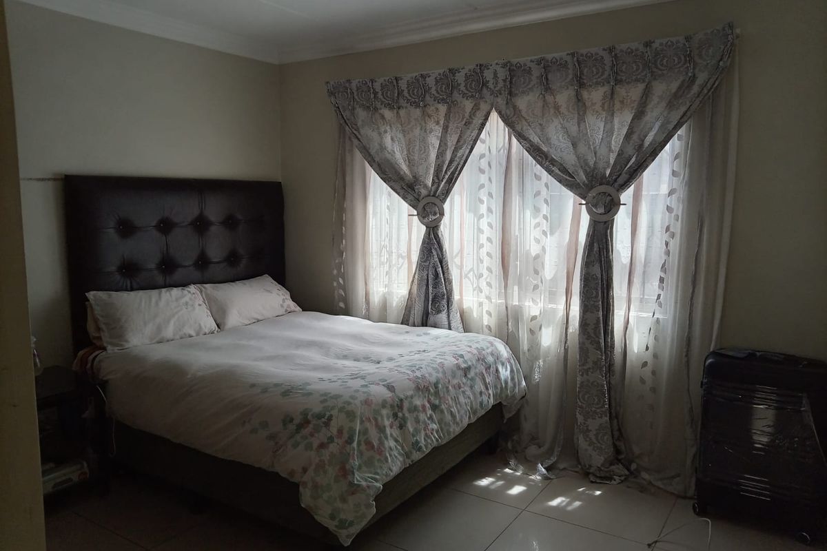 A bedroom featuring tiled flooring and decorative cornicing, illuminated by natural light through a window with curtains.