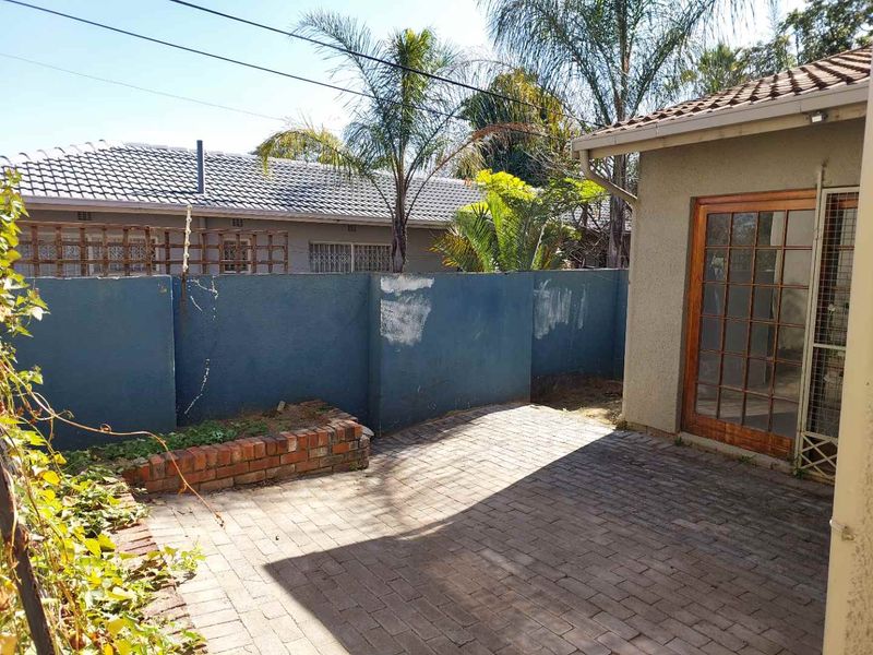 A private rear courtyard featuring paved flooring, a brick planter box, and a wooden framed glass door leading into the apartment.