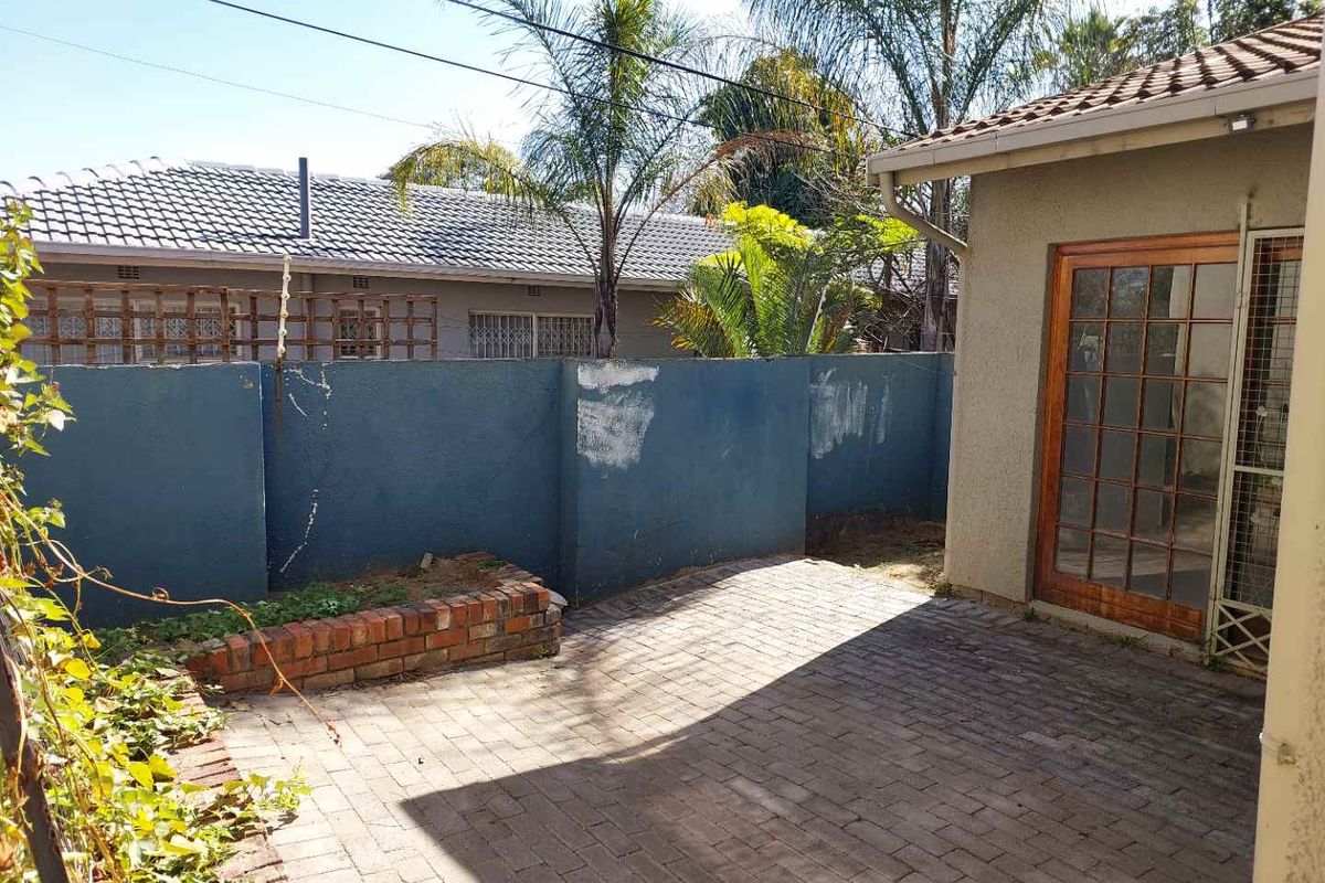 A private rear courtyard featuring paved flooring, a brick planter box, and a wooden framed glass door leading into the apartment.