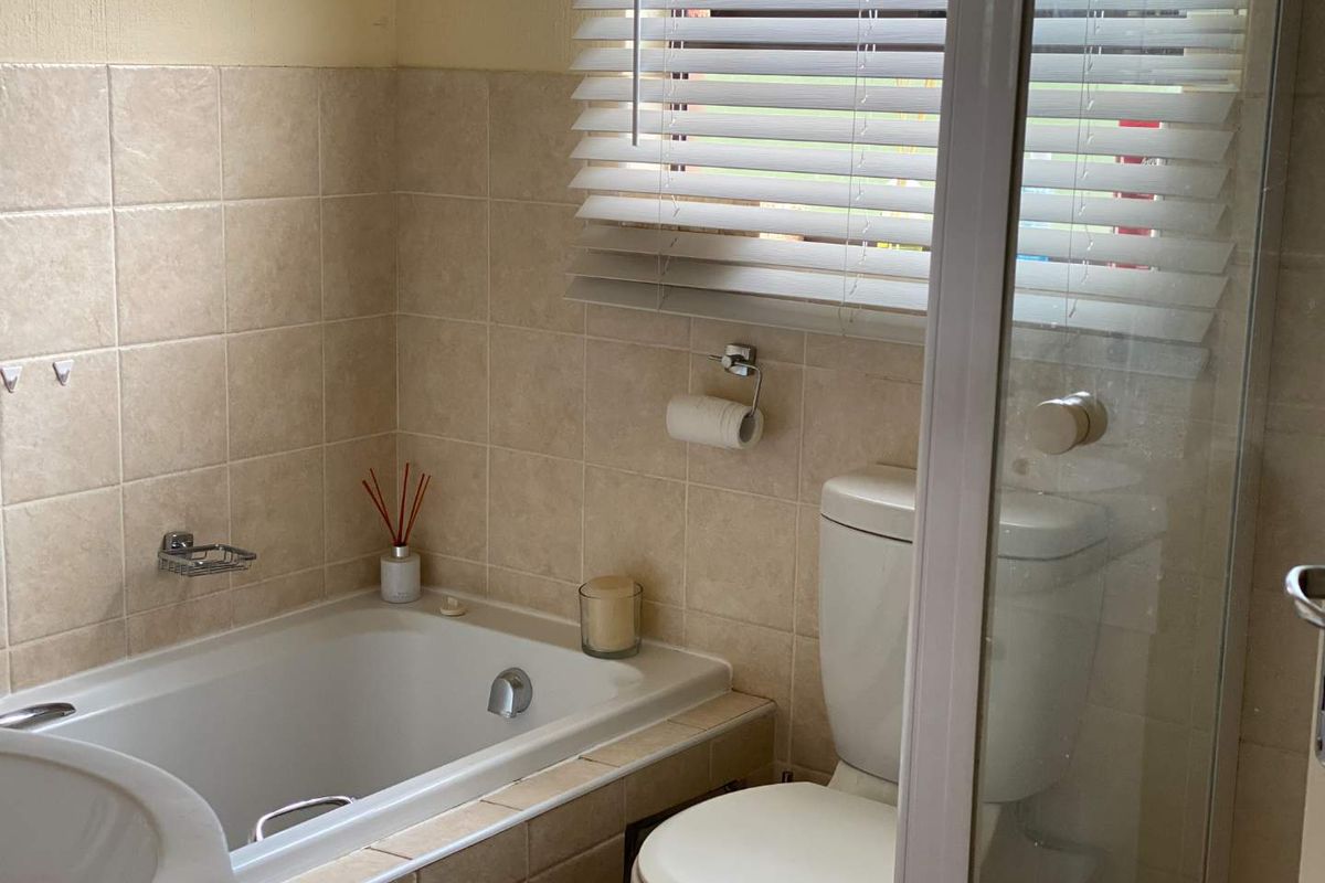 A functional bathroom featuring a built-in bathtub, a standard toilet, and a shower enclosure with tiled walls and window blinds.