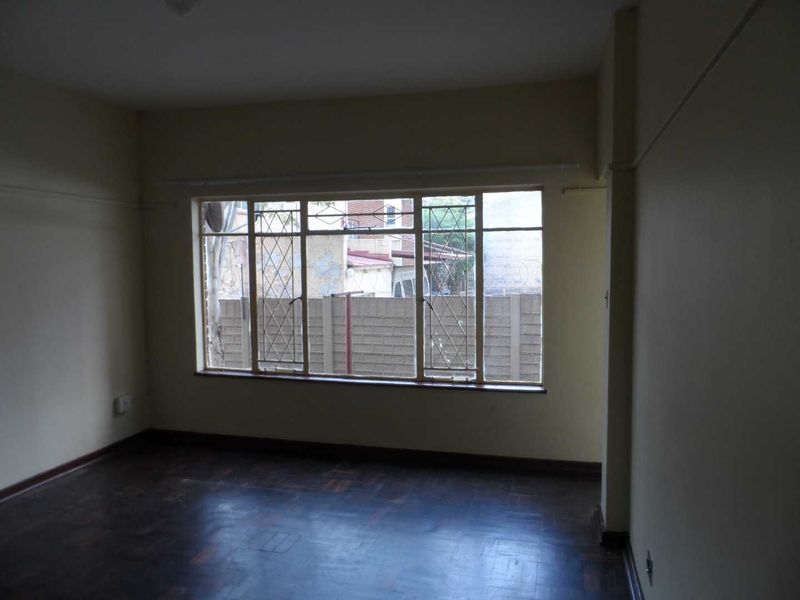 An empty living room featuring original parquet flooring and large steel-framed windows with security bars, offering a blank canvas for renovation.