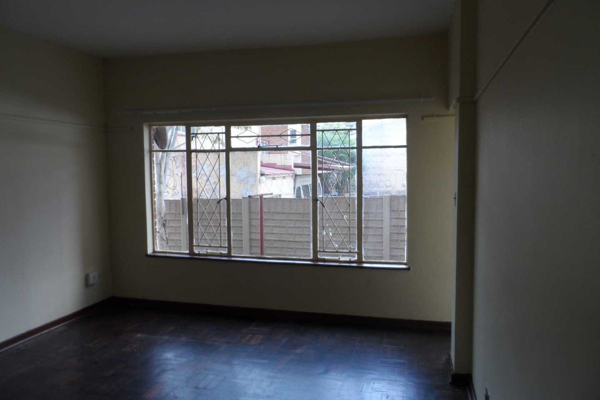 An empty living room featuring original parquet flooring and large steel-framed windows with security bars, offering a blank canvas for renovation.