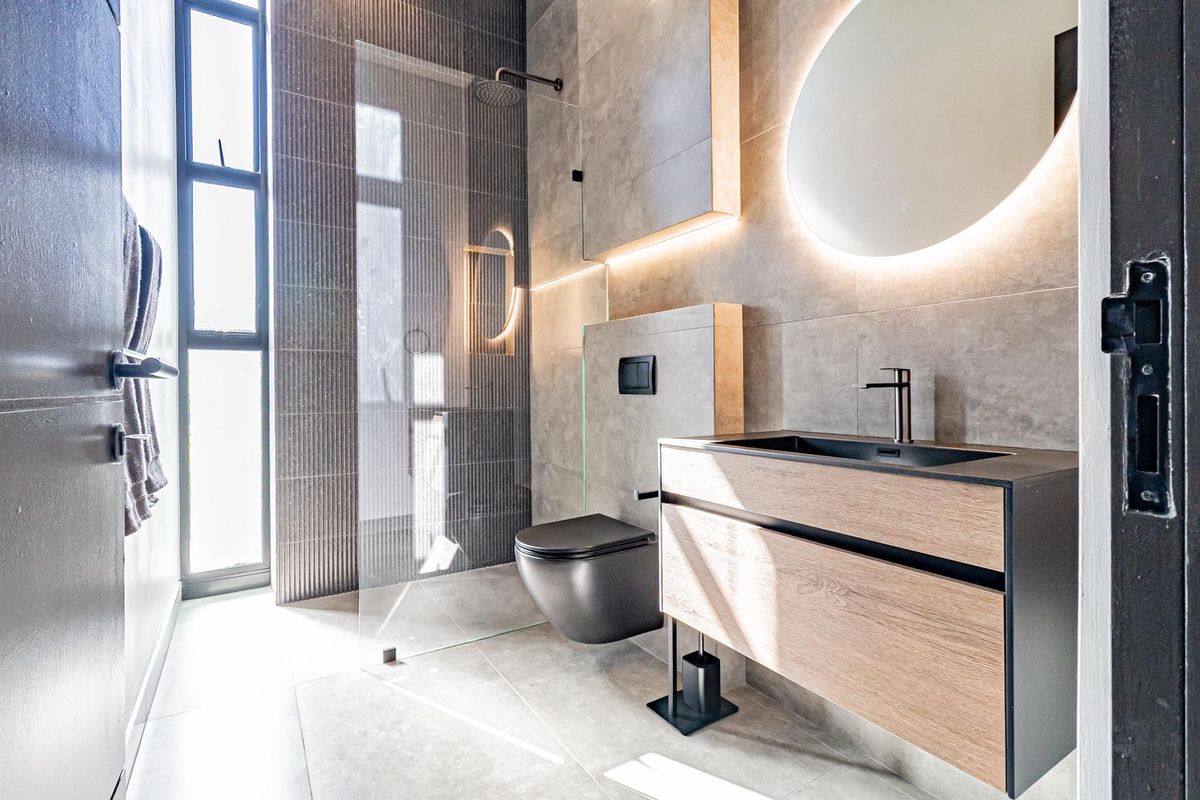 Modern bathroom featuring a floating vanity, wall-mounted toilet, walk-in glass shower, and contemporary tile finishes with integrated LED lighting.
