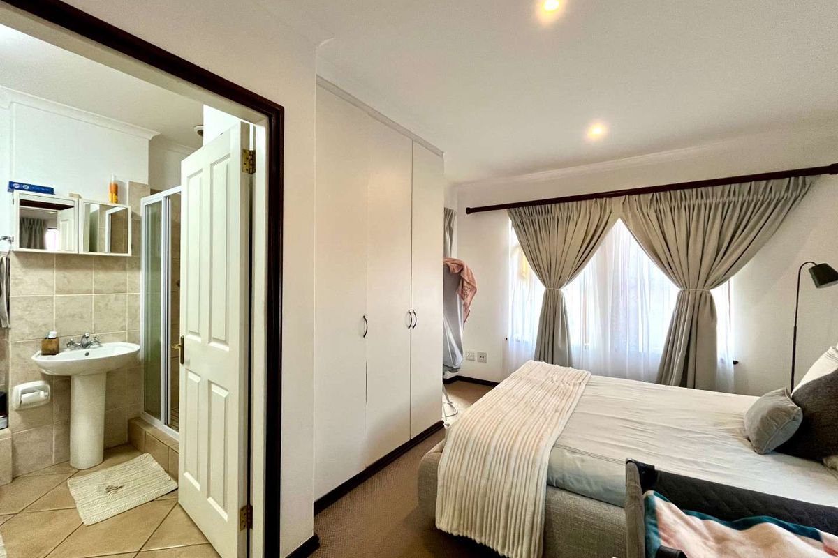 A bedroom featuring built-in cupboards and an attached en-suite bathroom with a pedestal basin and shower enclosure.
