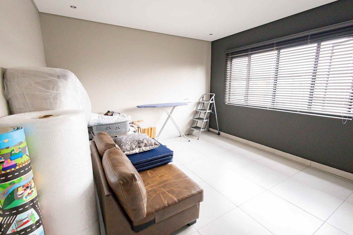 A bright bedroom featuring neutral wall tones, large windows with fitted blinds, and clean tiled flooring.