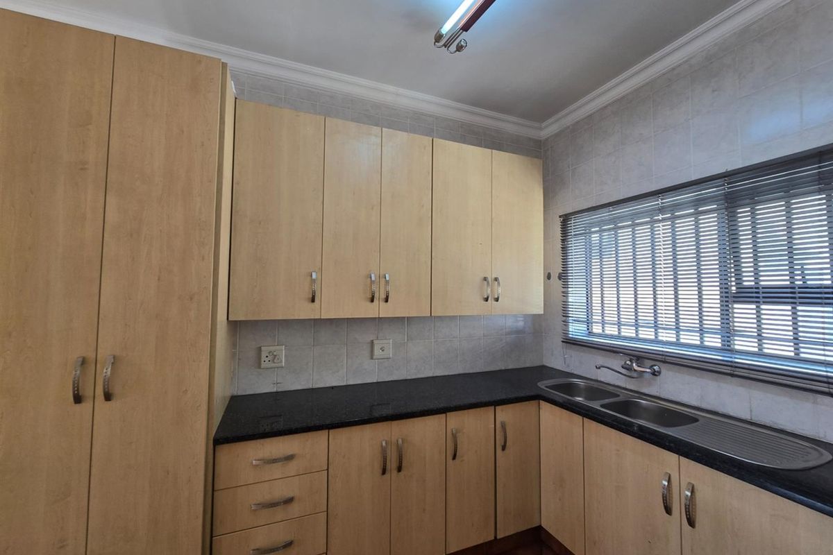 A functional kitchen featuring light wood-tone cabinetry, dark granite countertops, a double-basin stainless steel sink, and tiled wall finishes.