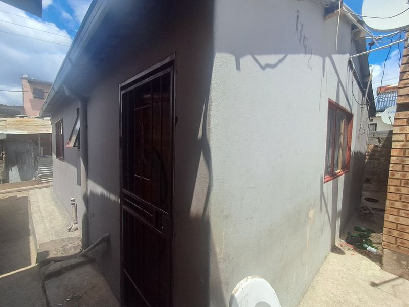 Rear exterior view of the property showing painted masonry walls, security gate, and window frames with visible signs of wear and maintenance requirements.
