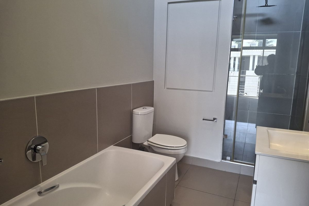 Modern bathroom featuring a bathtub, separate shower enclosure with rain shower head, toilet, and vanity basin with neutral wall and floor tiling.