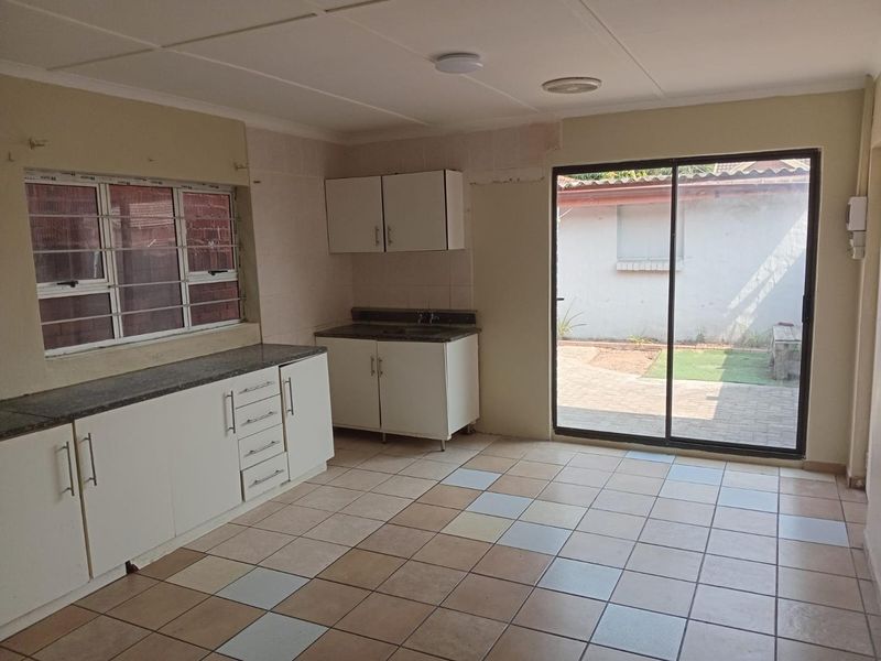 An empty kitchen featuring white built-in cabinetry, granite countertops, tiled flooring, and a sliding glass door providing direct access to the rear outdoor area.