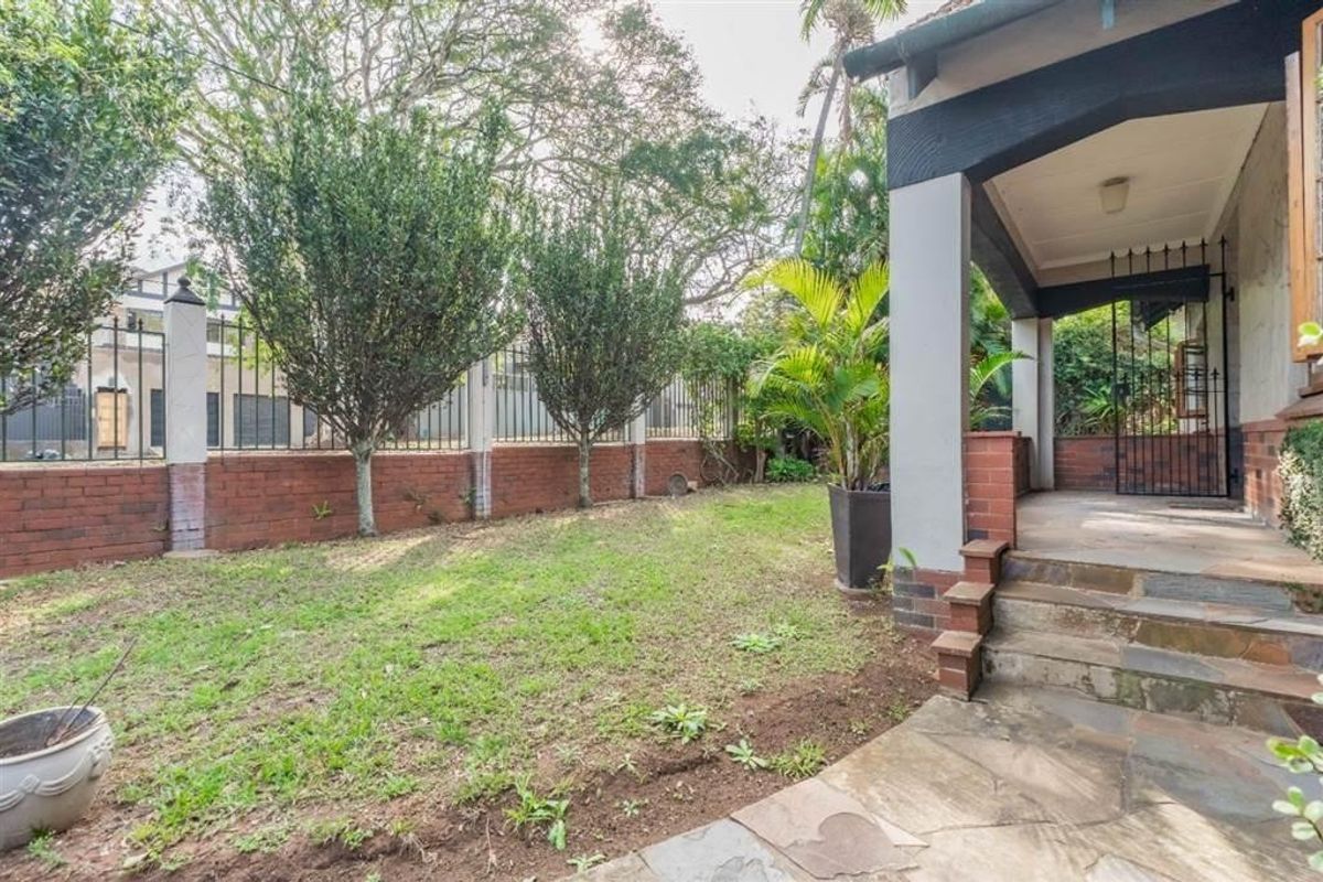 A rear garden area featuring a stone-paved patio, covered porch with brick steps, and a brick boundary wall with integrated security gate.