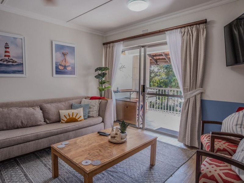 A bright living room featuring laminate flooring and a large sliding glass door that provides access to an outdoor balcony area.