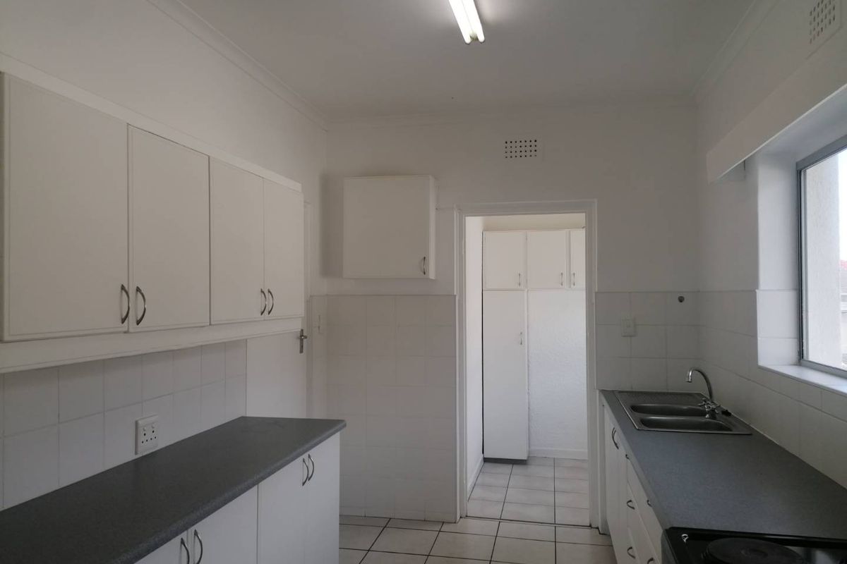 A functional, empty kitchen featuring white cabinetry, dark laminate countertops, tiled flooring, and a double bowl sink with an adjacent scullery area.