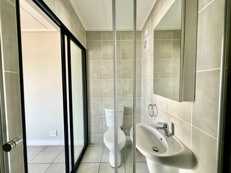 A clean, modern bathroom featuring neutral wall tiles, a pedestal basin, a toilet, and a wall-mounted mirror cabinet.