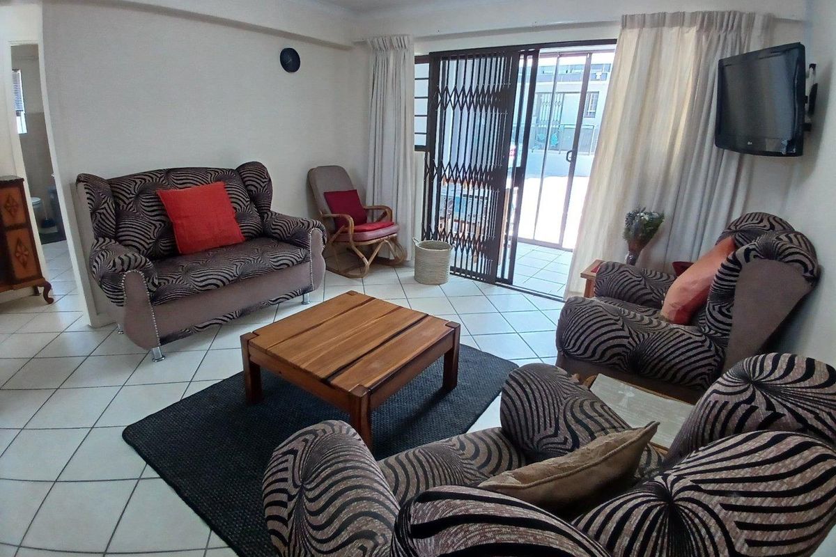 A living room featuring ceramic floor tiles and a sliding glass door with a security gate, providing access to an outdoor area.